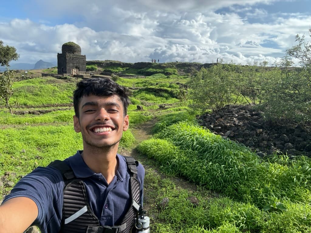 Portrait of Arnav Gupta smiling, outdoors on a green hillside
